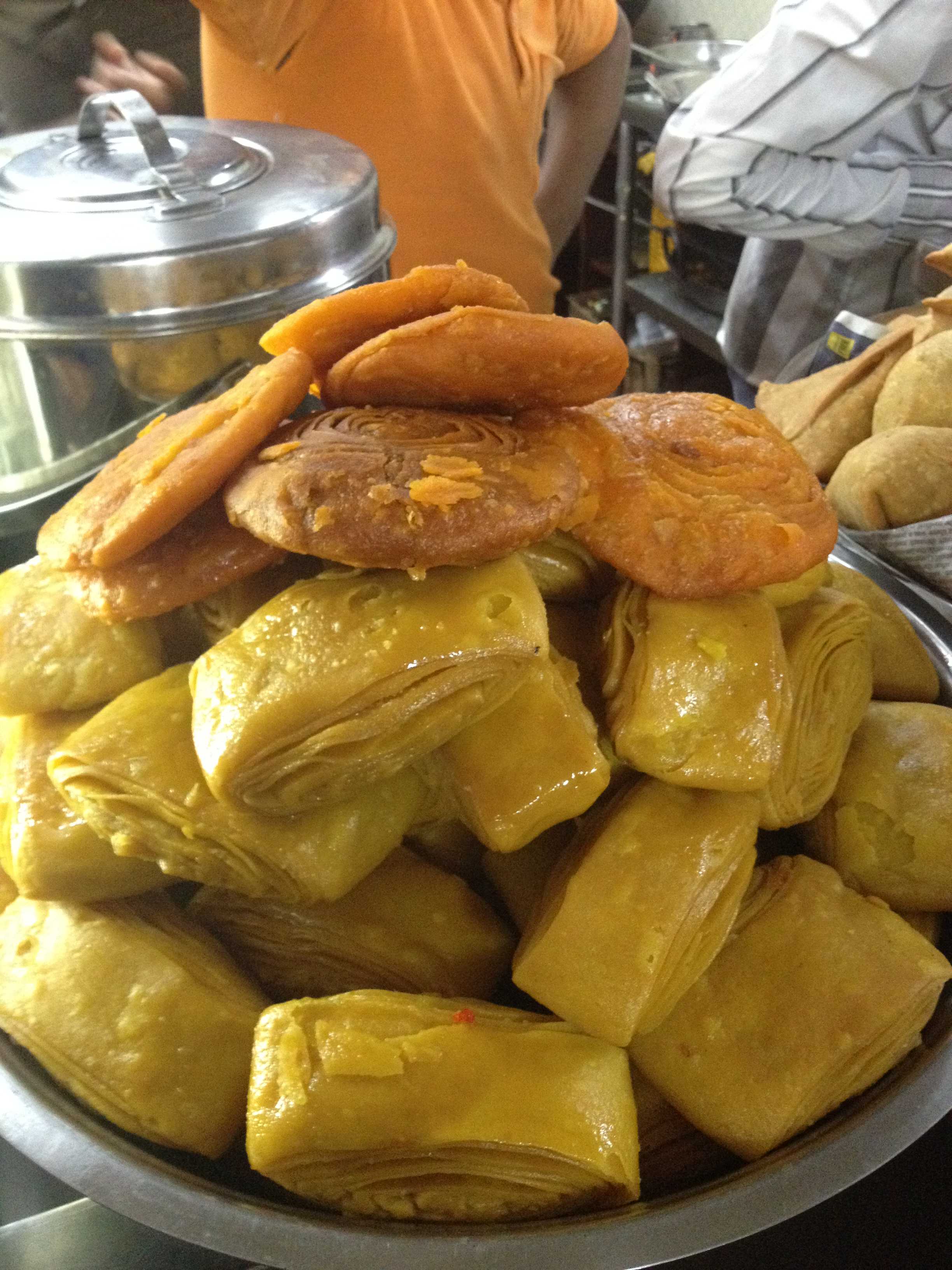 Close-up of a pile of golden fried pastries and snacks on a metal tray, warm yellow and orange tones