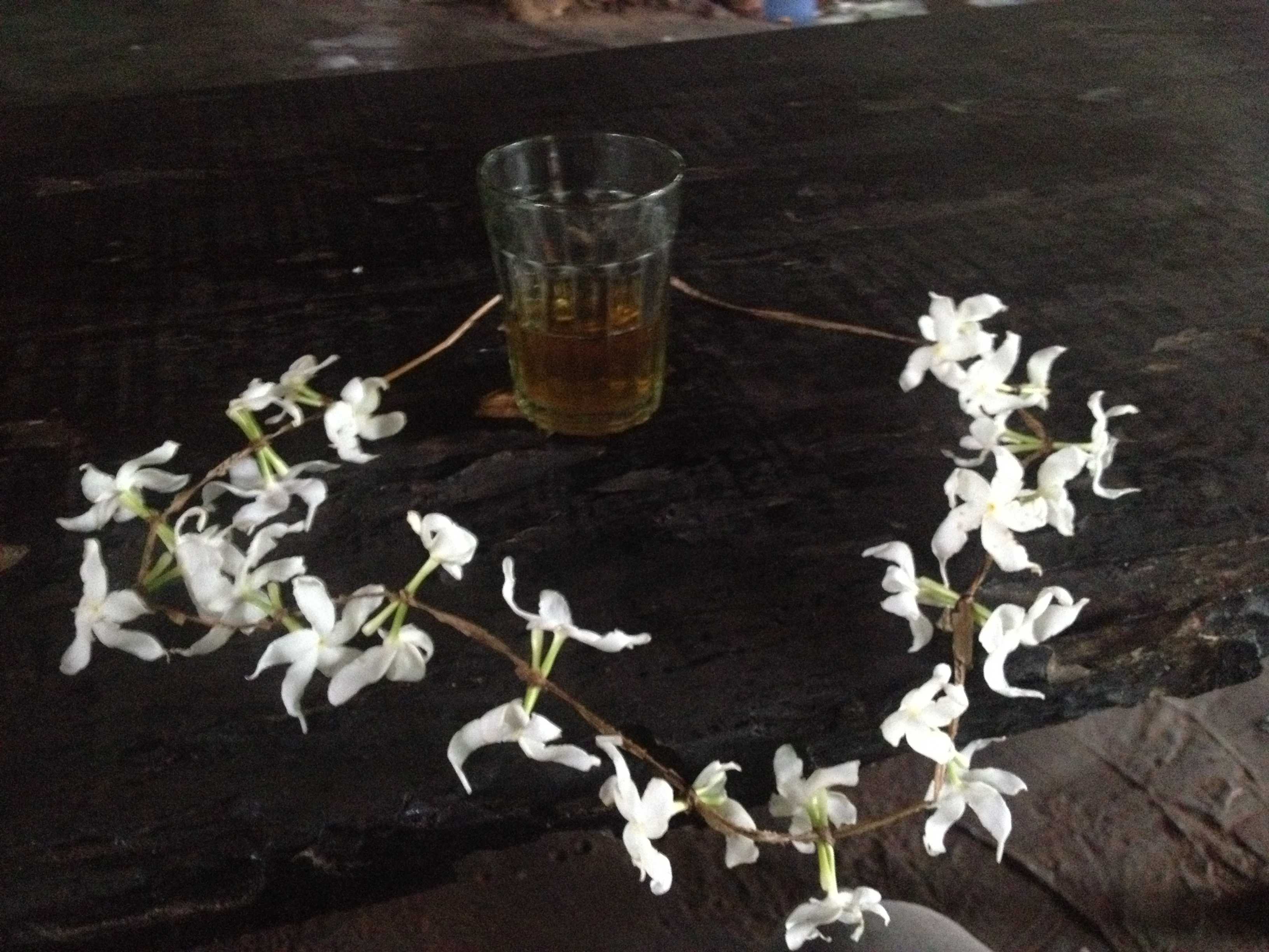 A glass of tea surrounded by a ring of small white flowers on a dark wooden surface